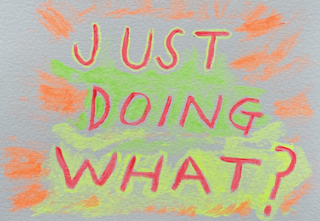 A plain white postcard that has "JUST DOING WHAT?" painted across it in neon red, orange, yellow and green.